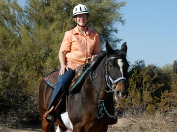 smiling woman in helmet riding horse