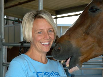 smiling volunteer with horse nibbling on her shoulder