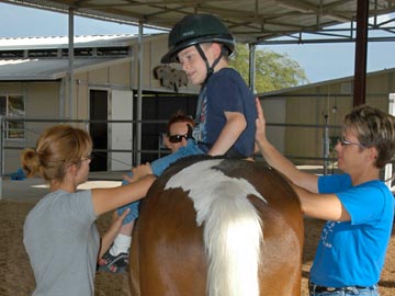 young boy student on horse with volunteers helping him dismount